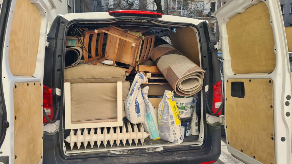 Otwarty bagażnik furgonetki załadowany gabarytami i odpadami z prac budowlanych. Wywóz odpadów po sprzątaniu.