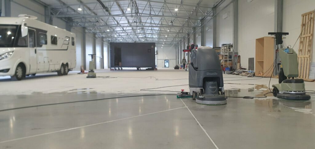 Czyszczenie szarej posadzki specjalistycznymi maszynami w obszernej hali salonu kamperów