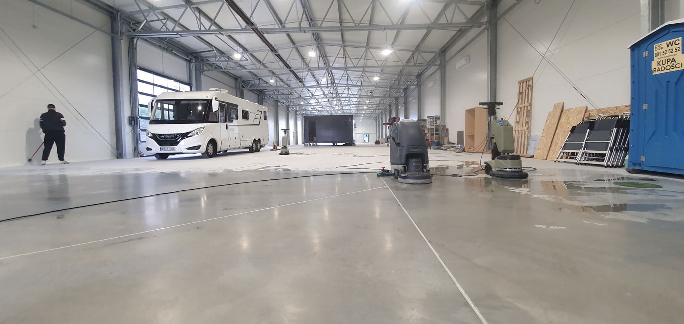 Czyszczenie posadzki w kolorze szarym w obszernej hali produkcyjnej