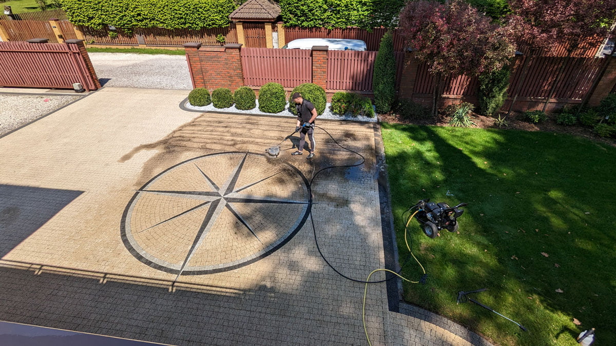 Jasna kostka brukowa silnie zabrudzona w trakcie czyszczenia przez pracownika firmySolid Work, specjalną maszyną, fragmenty już czyste wyglądają jak nowe