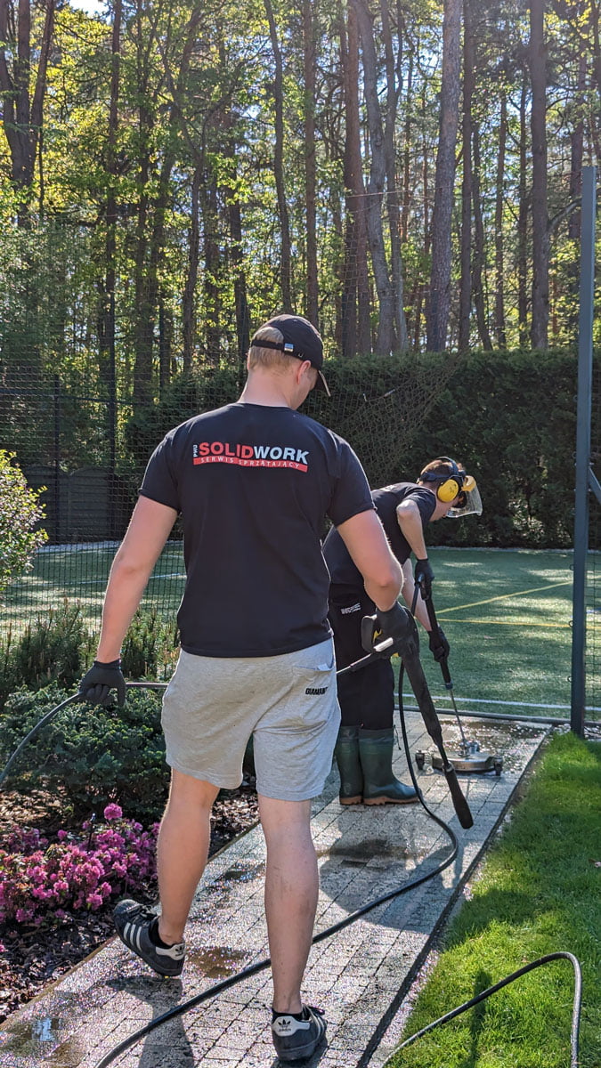 Mycie prowadzącej na boisko ścieżki z terakoty na obiekcie sportowym przez pracowników firmy Solid Work profesjonalnymi narzędziami