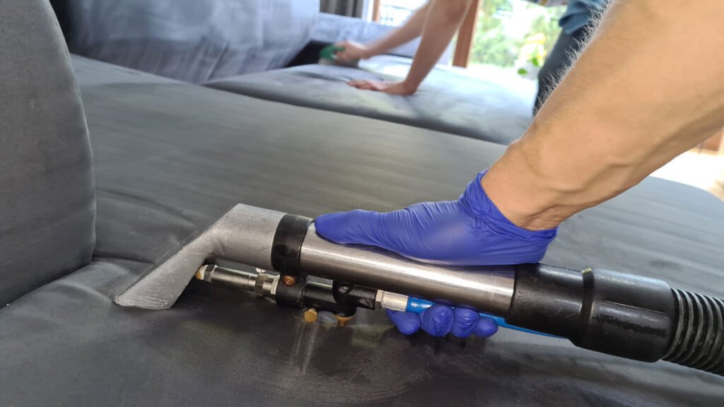 ręce pracowników w rękawiczkach lateksowych w trakcie odkurzania i czyszczenia tapicerowanych mebli w kolorze grafitowym