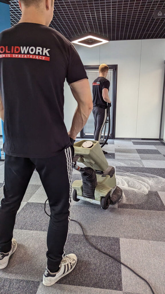 Pracownicy Solid Work piorą maszynami szarą wykładzinę w firmie SpotAWheel