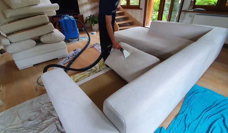 Odkurzanie fragmentu tapicerki białej kanapy. Mebel został całkowicie rozłożony do czyszczenia